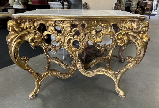 A beautiful carved and gilded center table. Decorated with openwork rocaille cartouches, palms and garlands. The falls, decorated with women in bust form, end in cambered legs joined by an x-shaped brace. Recessed pink veined white marble top, previously 