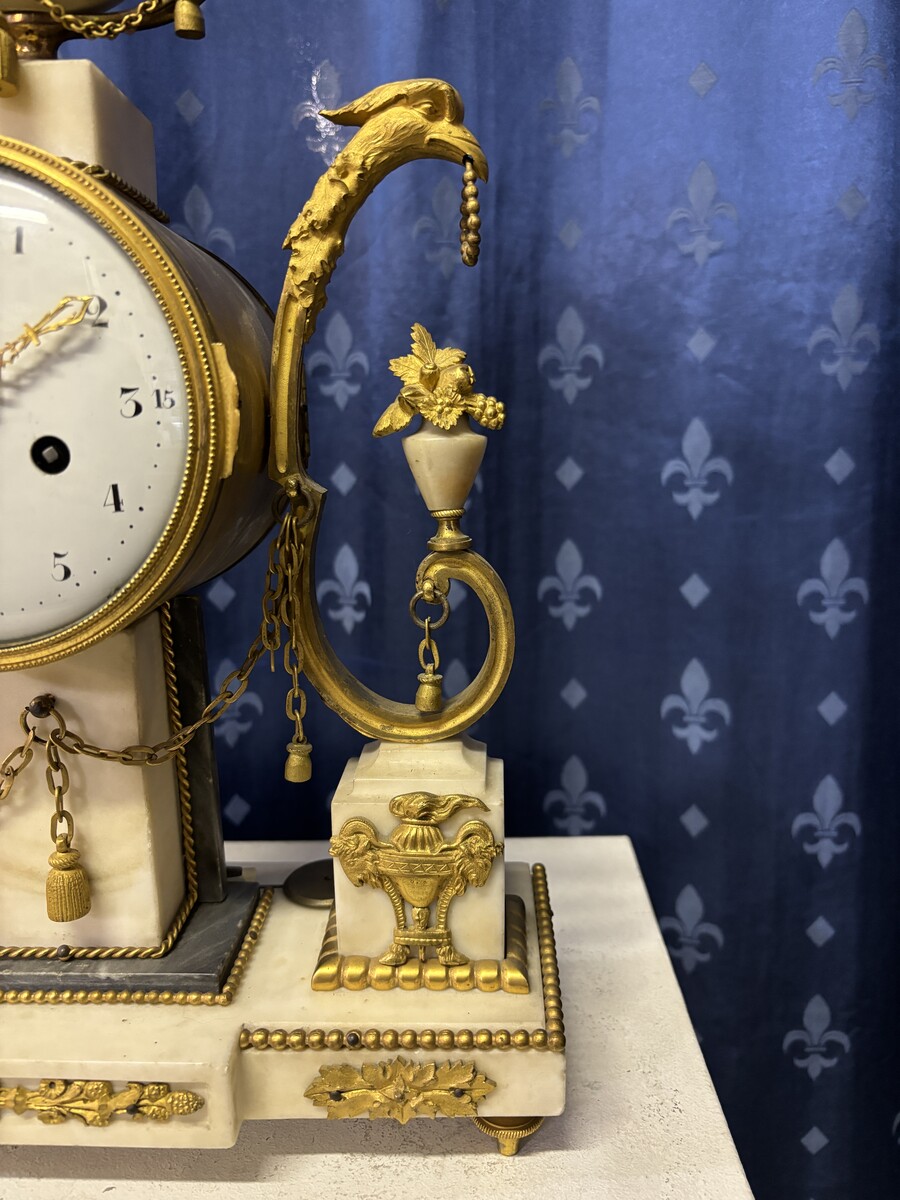 Elegant Louis XVI style clock from the 18th century. Beautiful 18th century marble and gilt bronze mantel clock decorated with vases of flowers, ornaments, griffin heads and bronze girlandes. The pendulum and key are present. 18thC.