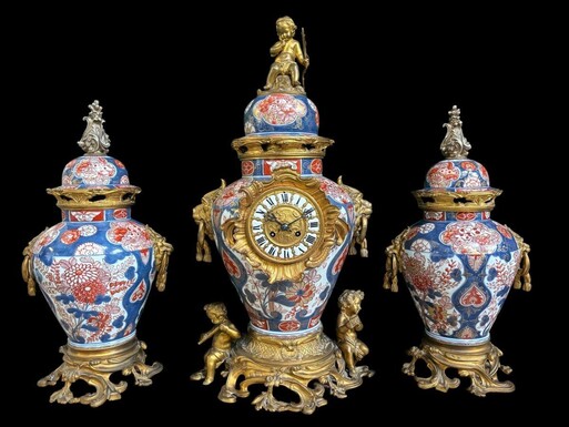 Large mantelpiece in porcelain and gilt bronze 19th century. Fireplace garniture comprising a large lidded vase/clock with 2 lidded vases in porcelain decorated with gilt bronze ornaments , lion heads and music-making putti. Key and pendulum present